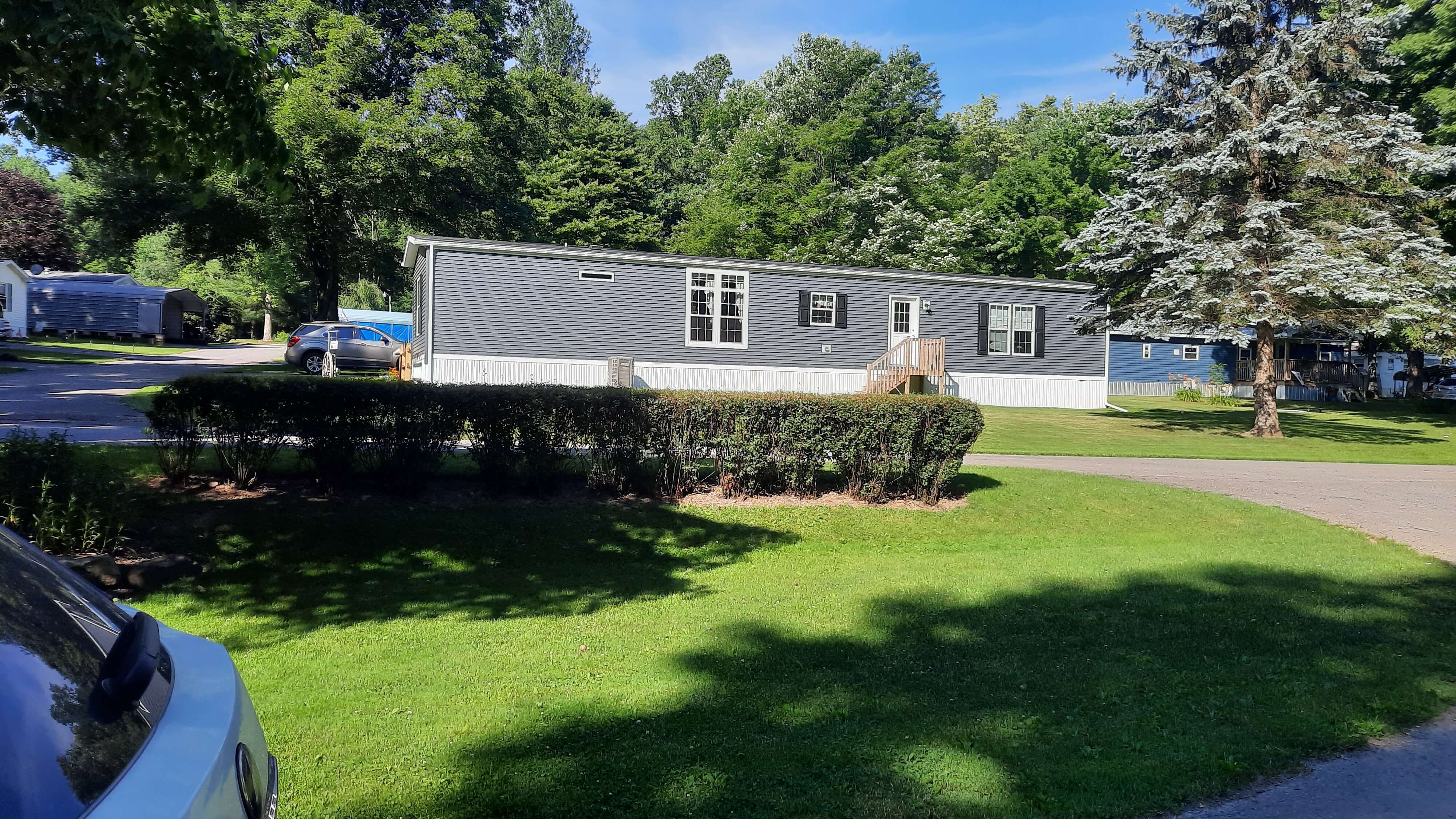 Photo from opposing yard of gray mobile home