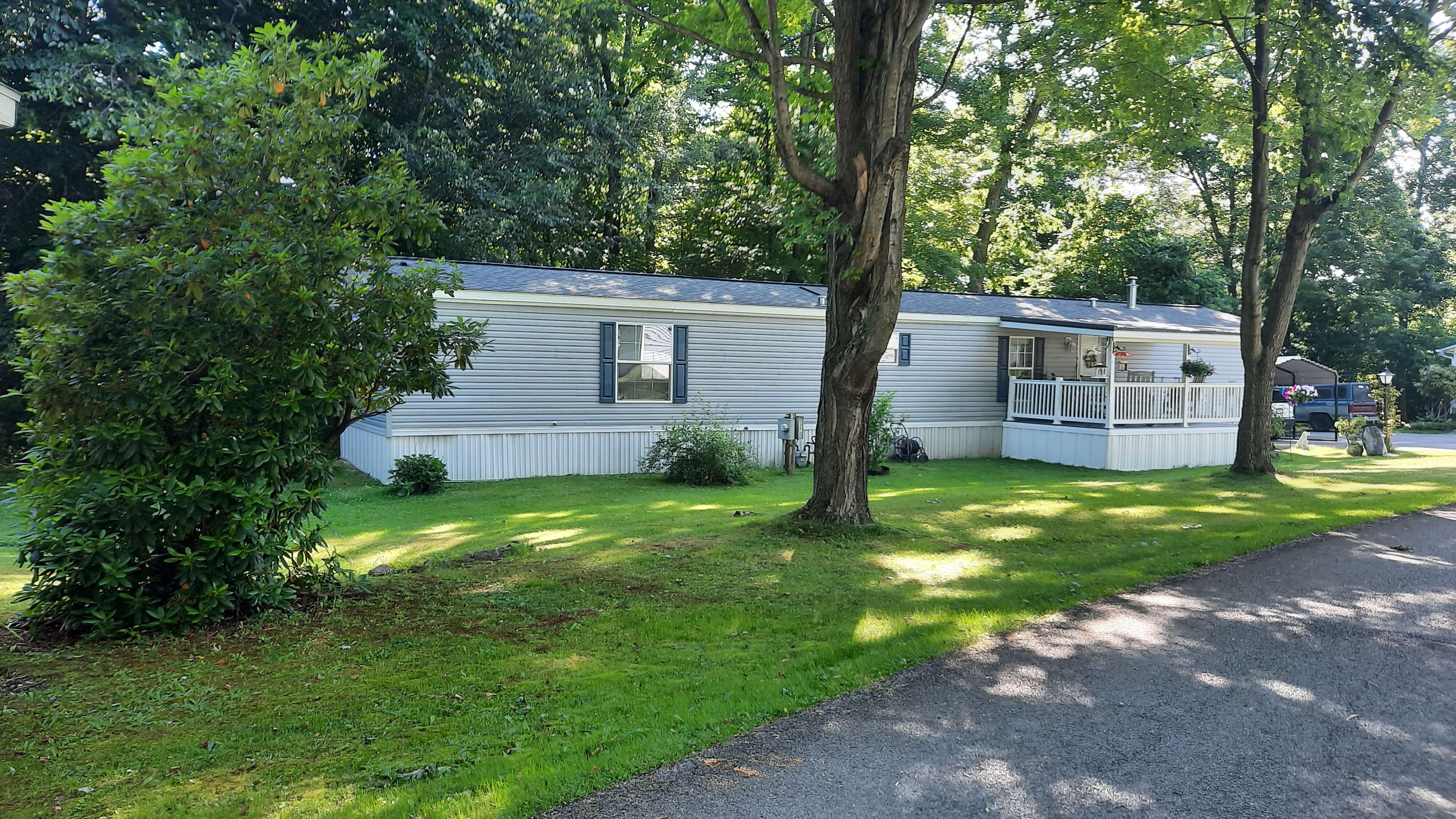 Gray mobile home with deck and yard containing trees