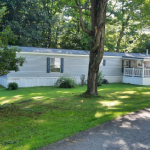 Gray mobile home with deck and yard containing trees icon