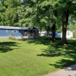 Blue mobile home with large yard and trees icon